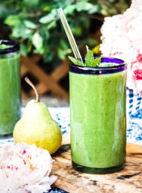 Fresh green smoothie in a glass with a straw, surrounded by pears and flowers.