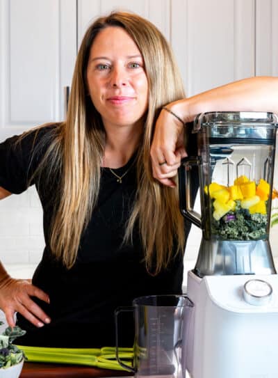 Woman preparing a healthy green smoothie with fruits and vegetables in a modern kitchen.