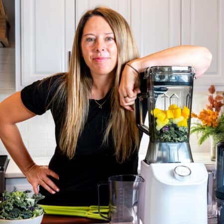 Woman preparing a healthy green smoothie with fruits and vegetables in a modern kitchen.