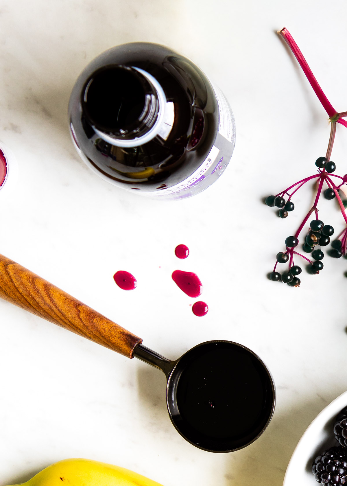 A glass bottle of dark purple elderberry syrup is pictured with a tablespoon full of the viscous liquid.