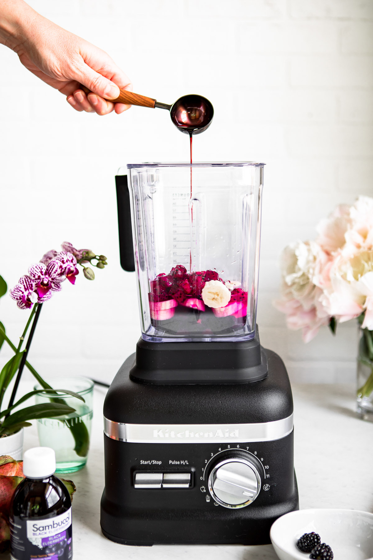 Elderberry syrup being poured into a blender with ingredients for a healthy smoothie.