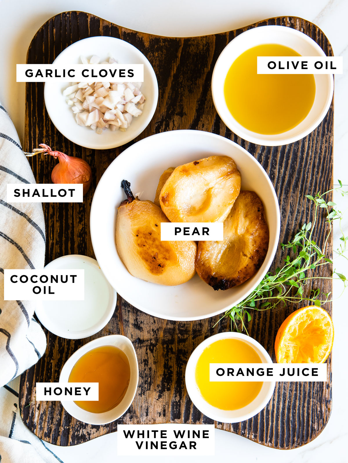 labeled ingredients for roasted pear vinaigrette including garlic cloves, olive oil, shallot, pear, coconut oil, honey, orange juice and white wine vinegar.