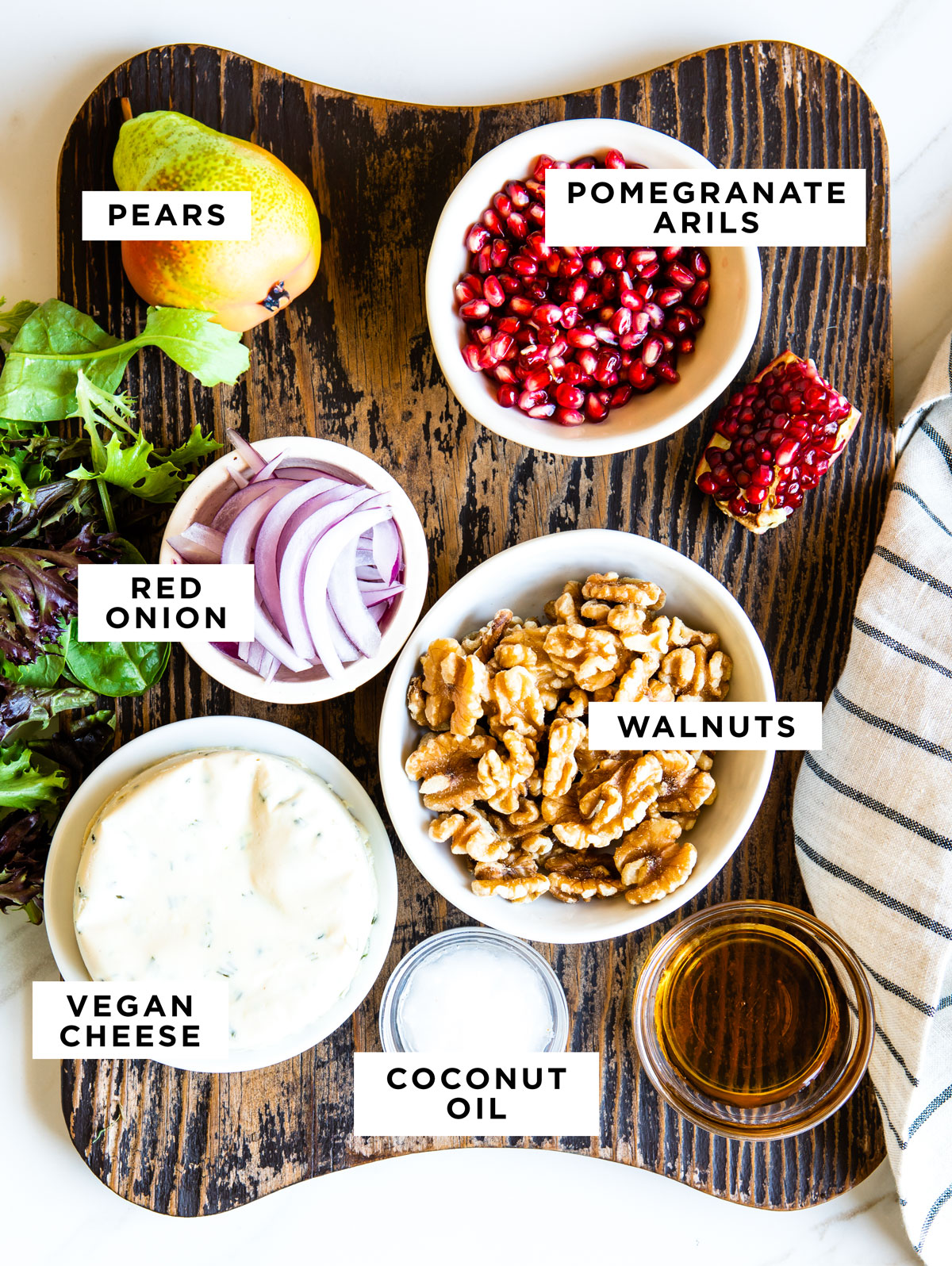 Gli ingredienti etichettati per un'insalata di pere includono pere, arilli di melograno, cipolla rossa, noci, formaggio vegano e olio di cocco. 