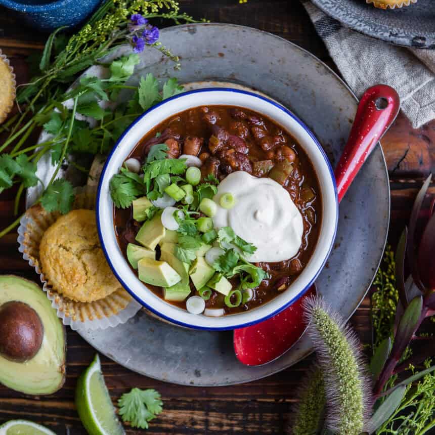 Bowl of chili topped with sour cream, avocado, and green onions.
