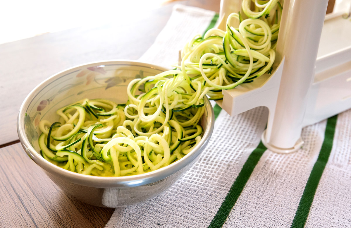 Spiralized zucchini noodles going into a bowl to make a recipe.
